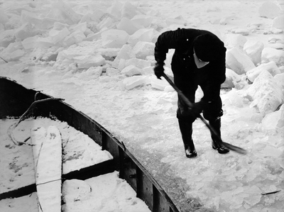 361186 Afbeelding van een man die een vastgevroren boot uit het ijs probeert te halen.